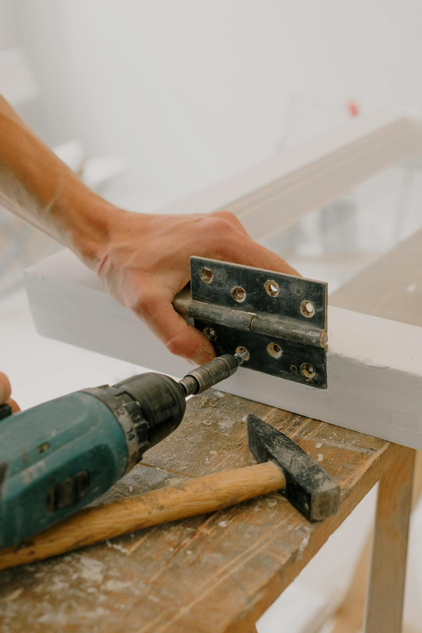 Crop unrecognizable craftsman attaching metal hinge with modern screwdriver on wooden window frame located on wooden board during renovation works