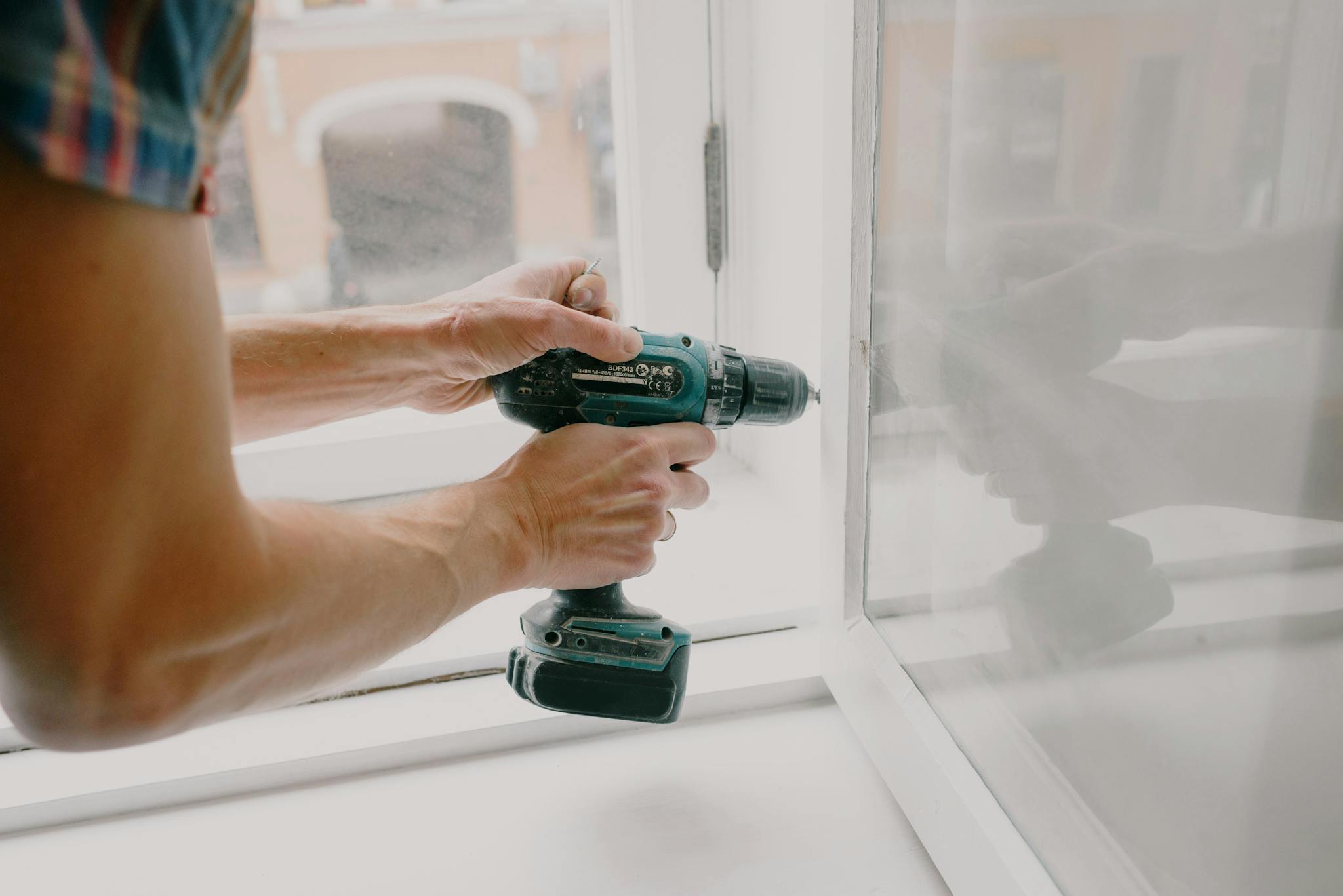 Side view of crop anonymous male mechanic fixing window with screwdriver during renovation process in apartment