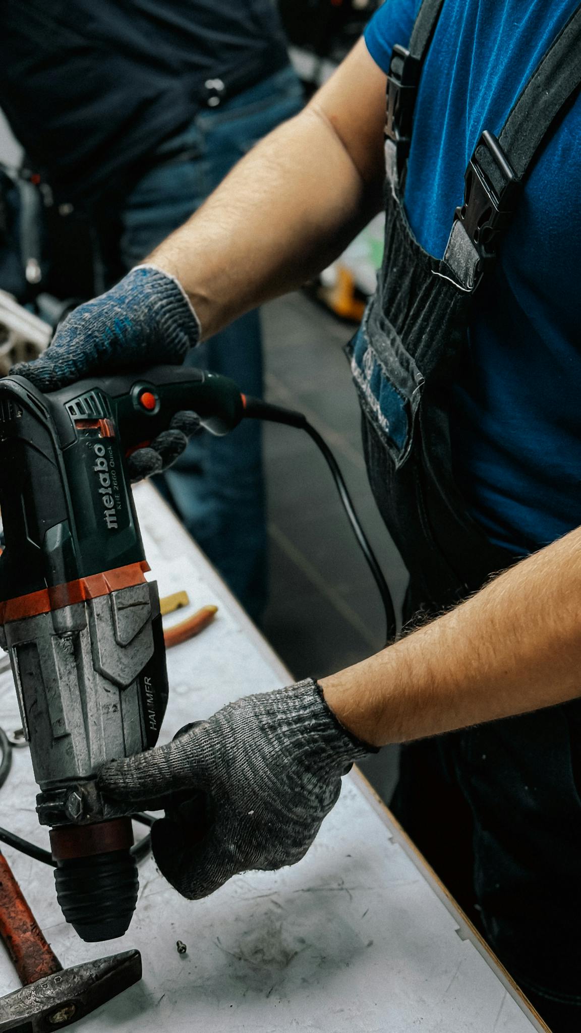 Worker operates an electric drill in a workshop, demonstrating carpentry tools and skills.